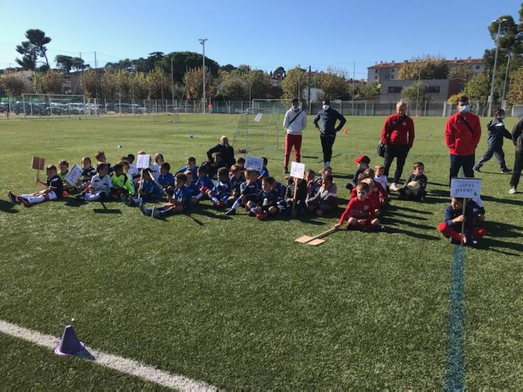 Un groupe d'enfants et d'adultes posent sur un terrain de football ensoleillé.