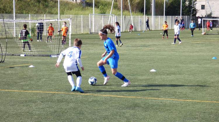 Des jeunes joueurs et joueuses de football s'entraînent sur un terrain en herbe synthétique sous un ciel ensoleillé.