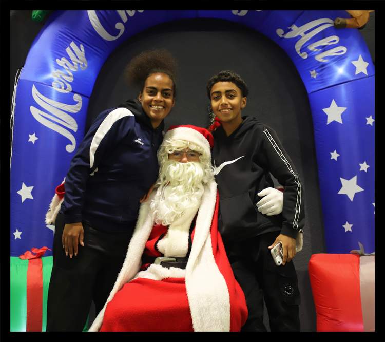 Deux jeunes souriants posent avec le Père Noël devant une arche décorée de Noël.