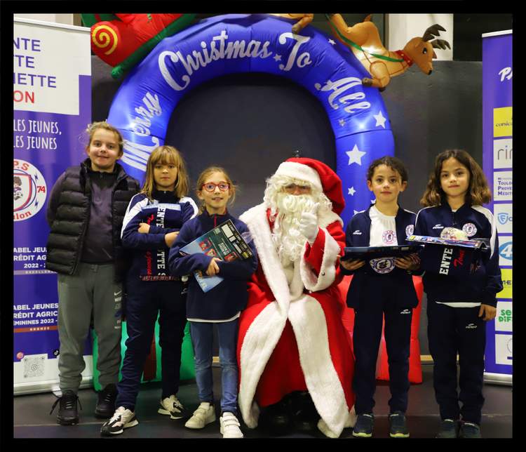 Le Père Noël pose avec des enfants devant une arche gonflable de Noël et des banderoles.
