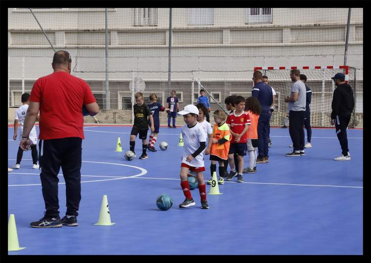 Des enfants et des adultes participent à un entraînement de football en salle avec des cônes et des ballons.