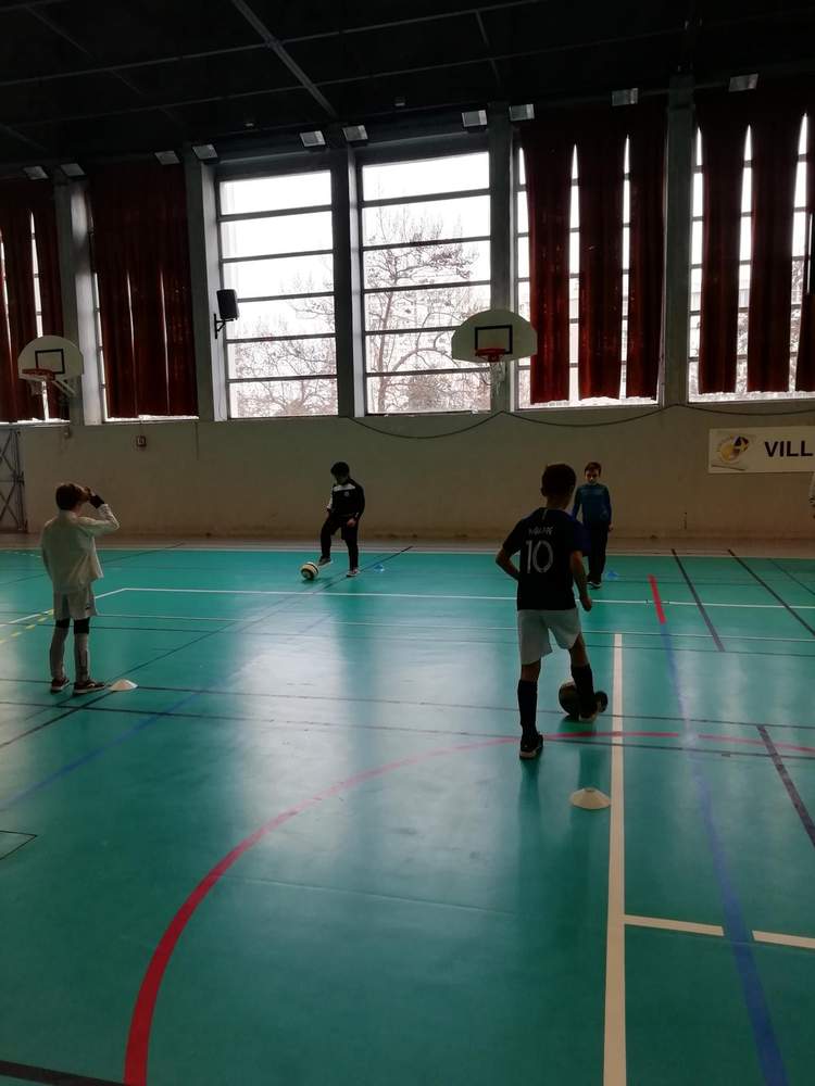 Des jeunes joueurs de football s'entraînent en salle avec des ballons et des cônes.
