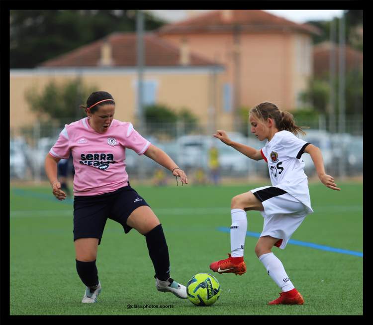Deux jeunes joueuses de football en pleine action sur un terrain vert, l'une en rose et l'autre en blanc, disputant le ballon.