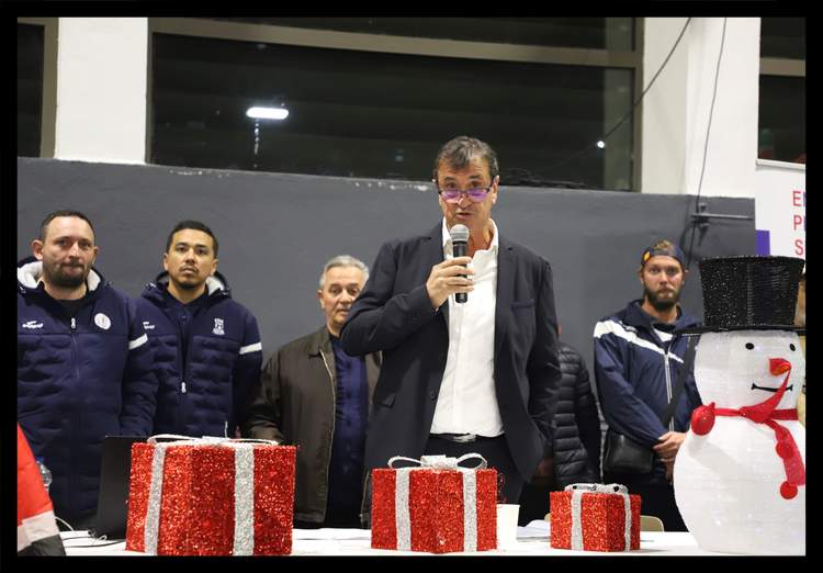 Un homme parle au micro devant un groupe de personnes et des décorations de Noël.