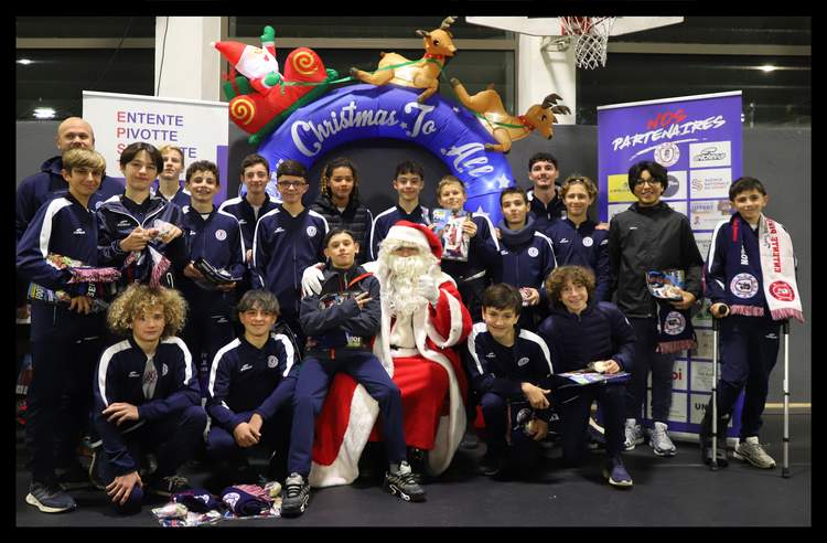 Un groupe de jeunes footballeurs pose avec le Père Noël devant une arche décorative de Noël et des bannières de partenaires.