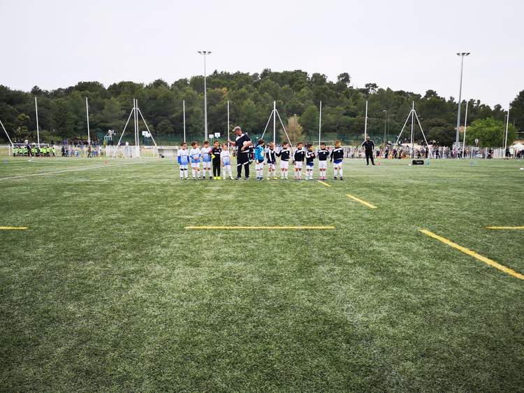 Une équipe de jeunes footballeurs en tenue, alignée sur un terrain de football synthétique, avec un entraîneur au centre.