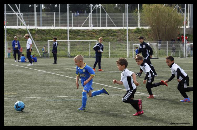 De jeunes footballeurs en pleine action sur le terrain, avec des adultes en arrière-plan.