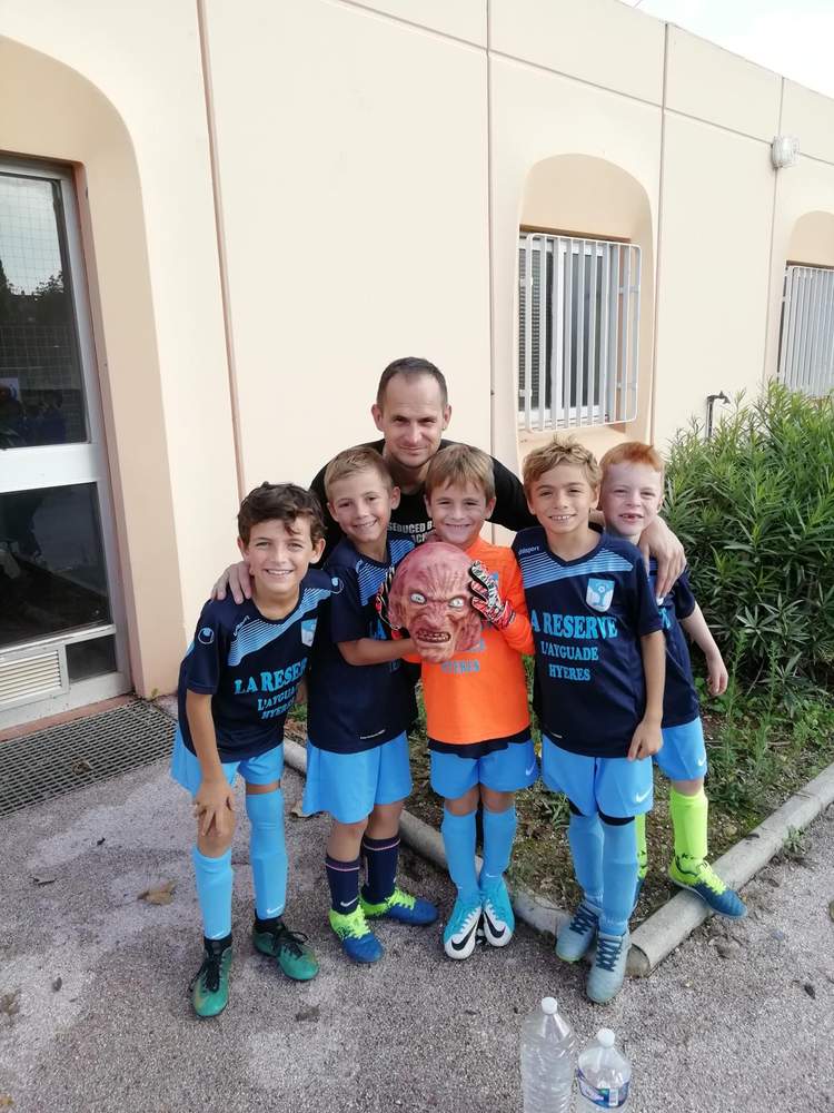 Un entraîneur et cinq jeunes joueurs de football posent avec un masque effrayant.