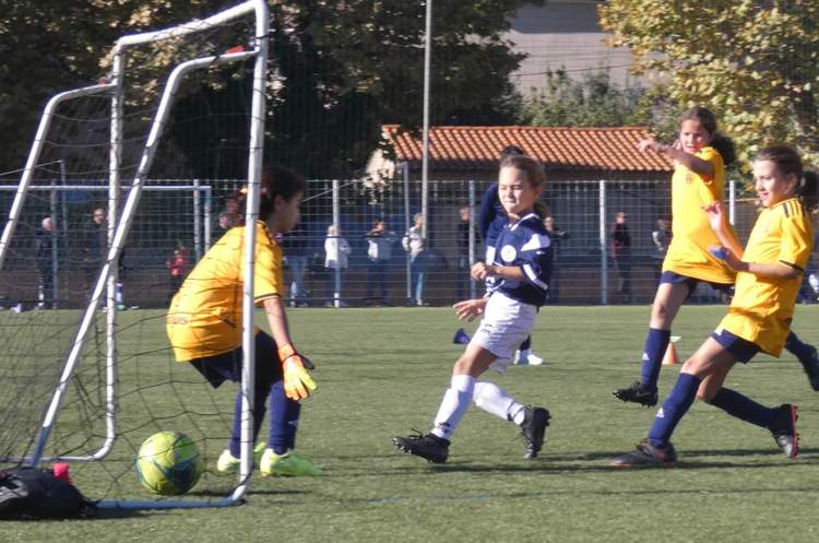 Des jeunes joueuses de football en pleine action sur le terrain, avec une gardienne devant le but.