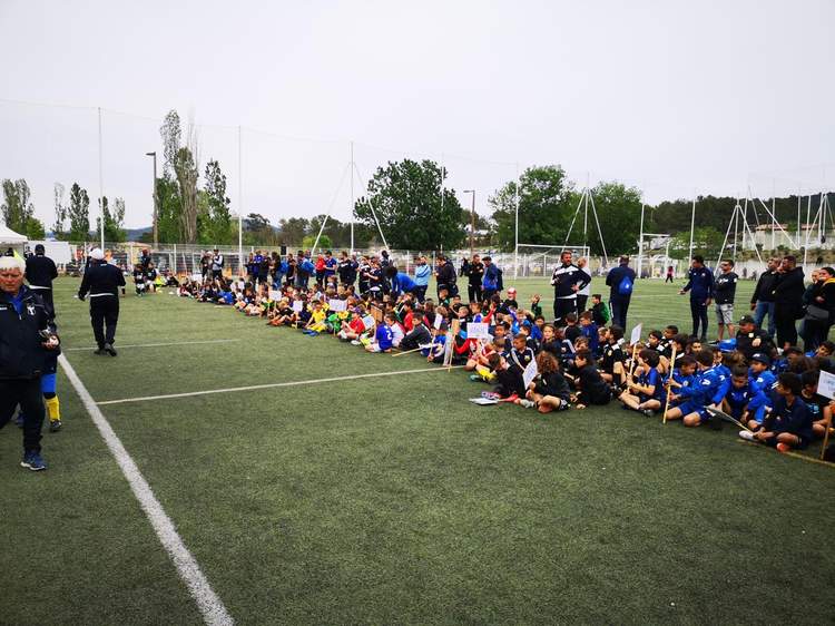 De nombreux jeunes joueurs de football sont assis sur le terrain, écoutant des adultes debout, lors d'un événement sportif.