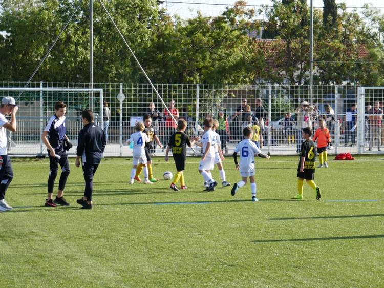 Des jeunes joueurs de football s'entraînent sur un terrain en gazon synthétique sous un ciel ensoleillé.