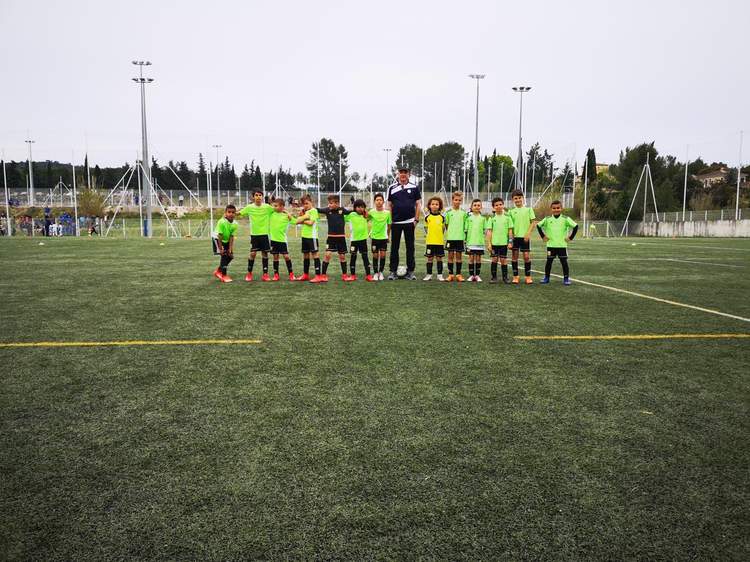 Une équipe de jeunes footballeurs et leur entraîneur posent sur un terrain de football en gazon synthétique.