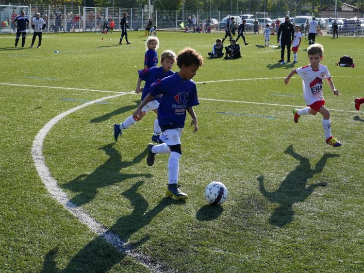 Des jeunes joueurs de football en pleine action sur un terrain synthétique ensoleillé.