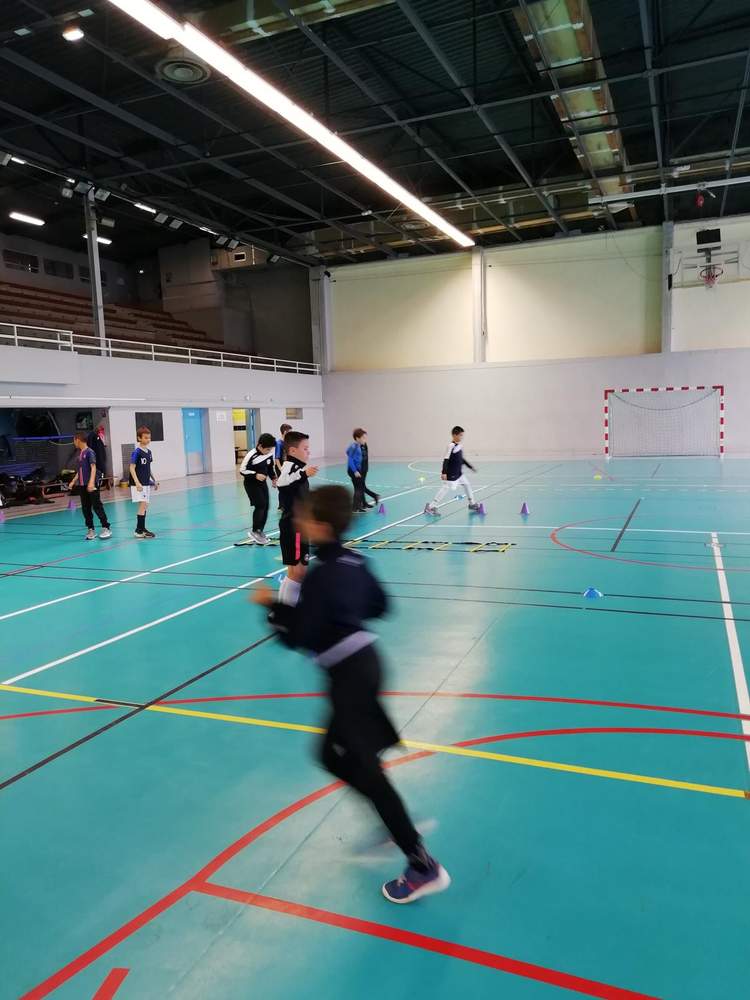 Des jeunes joueurs de football s'entraînent en salle, avec un joueur en mouvement au premier plan.