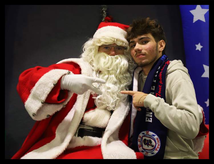 Un jeune homme avec une écharpe de club pose avec le Père Noël lors d'un événement festif.