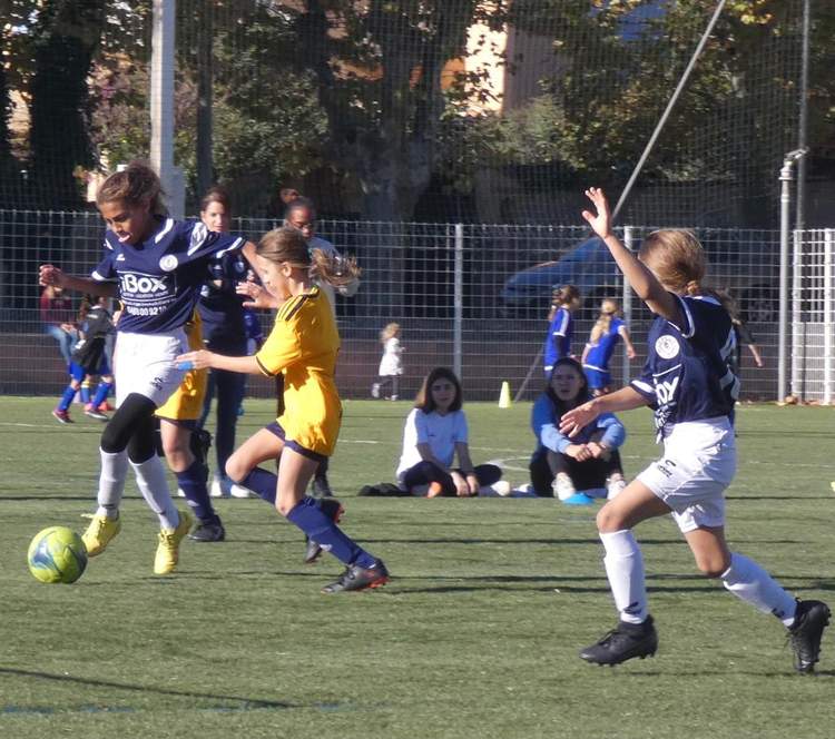 Des jeunes filles jouent au football sur un terrain en herbe sous un soleil éclatant.