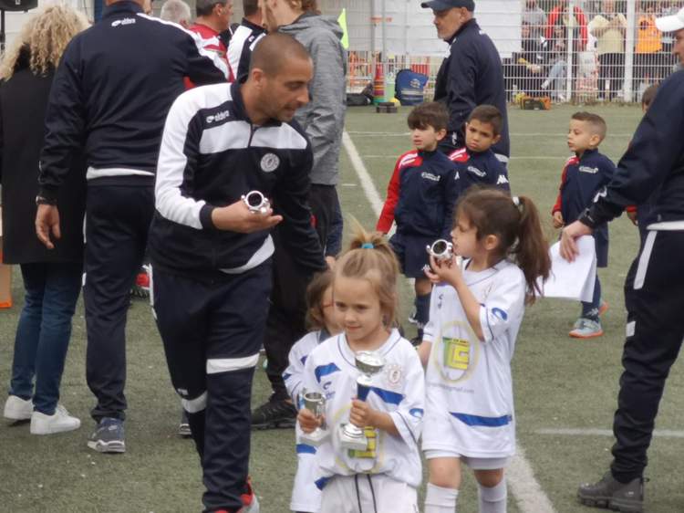 Des enfants et des adultes sur un terrain de football, certains enfants tenant des trophées.