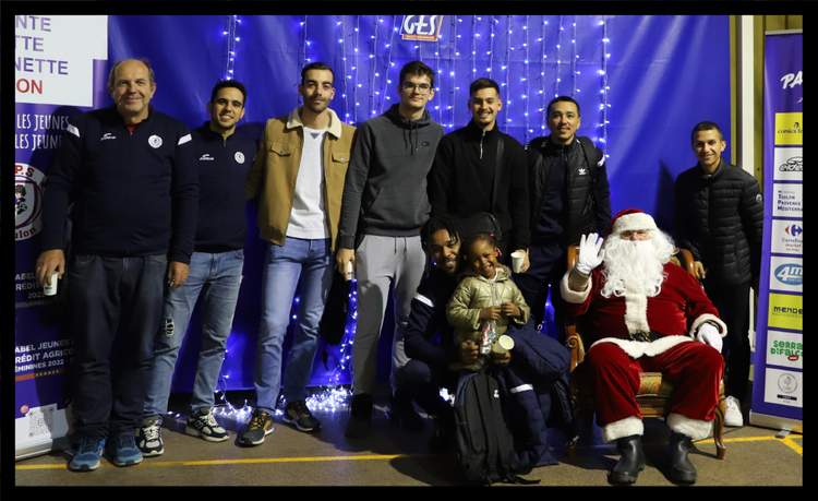 Un groupe d'hommes et un enfant posent avec le Père Noël devant un fond bleu décoré de lumières.