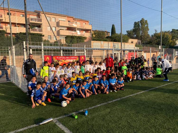 Une grande équipe de jeunes footballeurs et leurs entraîneurs posent sur le terrain de football.