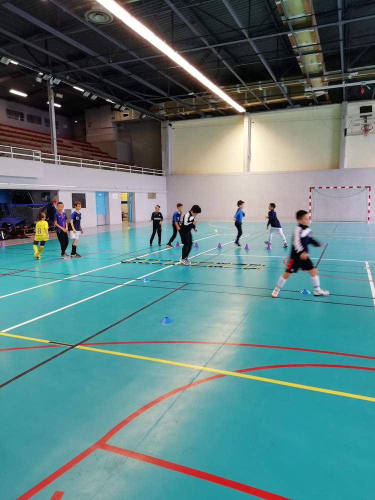 Des jeunes joueurs de football s'entraînent en salle sur un parcours d'agilité.