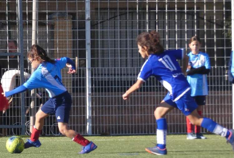 Deux jeunes joueurs de football en pleine action sur le terrain, avec d'autres personnes en arrière-plan.