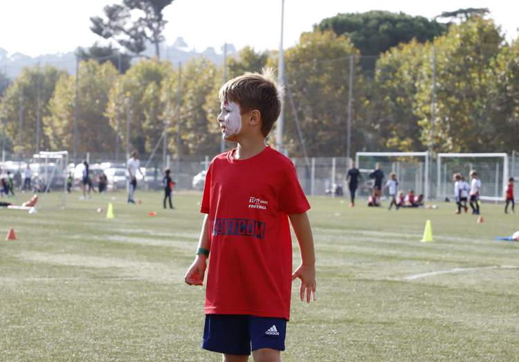 Un jeune garçon avec le visage maquillé regarde sur le côté sur un terrain de football ensoleillé.