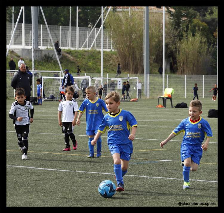 Des jeunes joueurs de football en maillot bleu et blanc s'entraînent sur un terrain vert, avec un ballon bleu au premier plan.