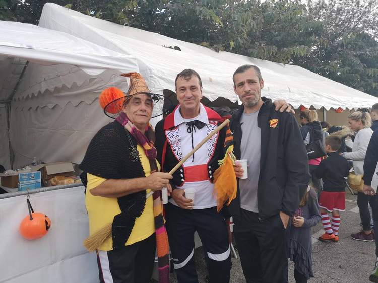 Trois hommes souriants, dont deux déguisés, posent devant une tente lors d'un événement festif.