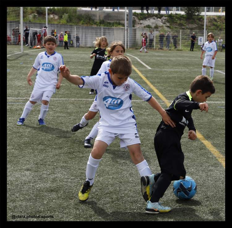 Des jeunes joueurs de football en pleine action sur le terrain, un enfant dribblant le ballon tandis qu'un autre tente de le lui prendre.