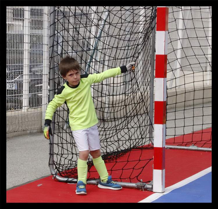 Un jeune gardien de but en tenue fluo pose devant un but de football en salle.