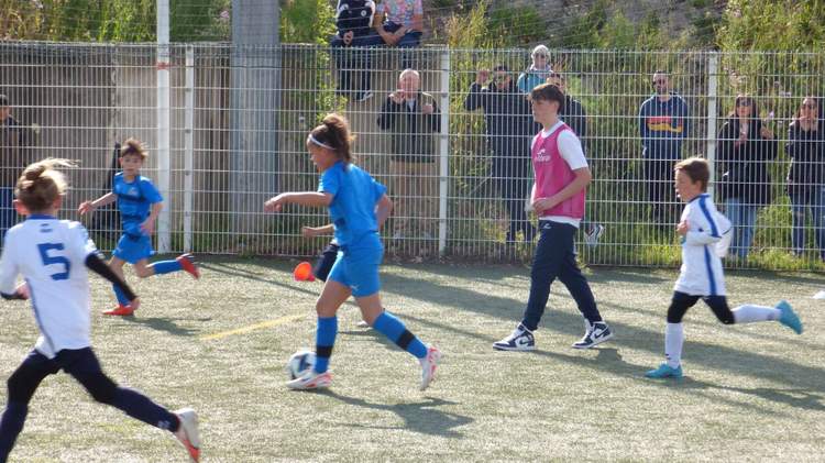 Des jeunes joueurs de football en pleine action sur un terrain, avec des spectateurs en arrière-plan.
