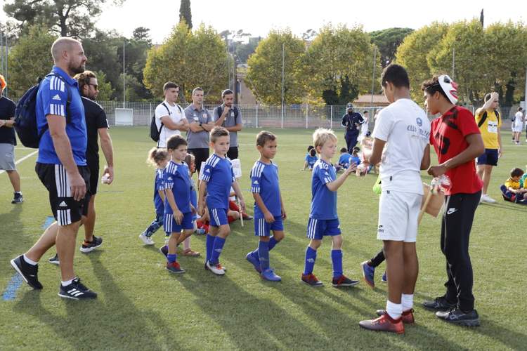 Des jeunes joueurs de football en tenue bleue écoutent des adultes sur un terrain en herbe.