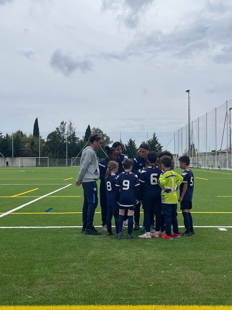 Un groupe de jeunes footballeurs et leurs entraîneurs se rassemblent sur un terrain de football en gazon synthétique.