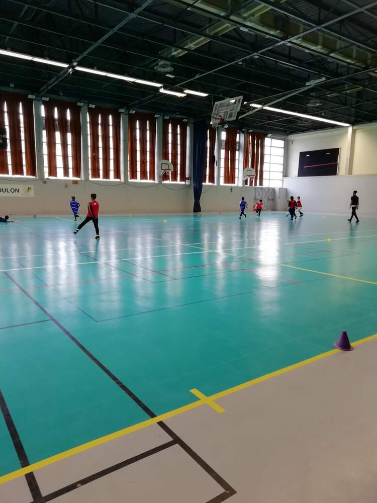 Des jeunes joueurs s'entraînent au football en salle sur un terrain vert et gris.