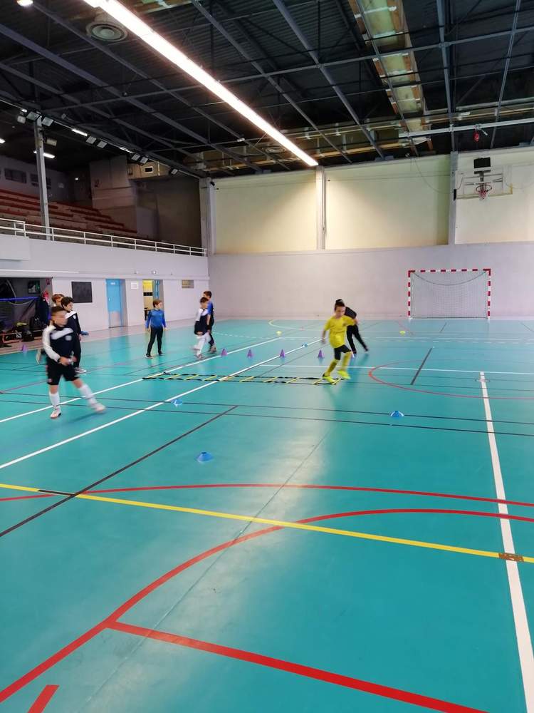 Des jeunes joueurs de football s'entraînent en salle avec des cônes et une échelle d'agilité.