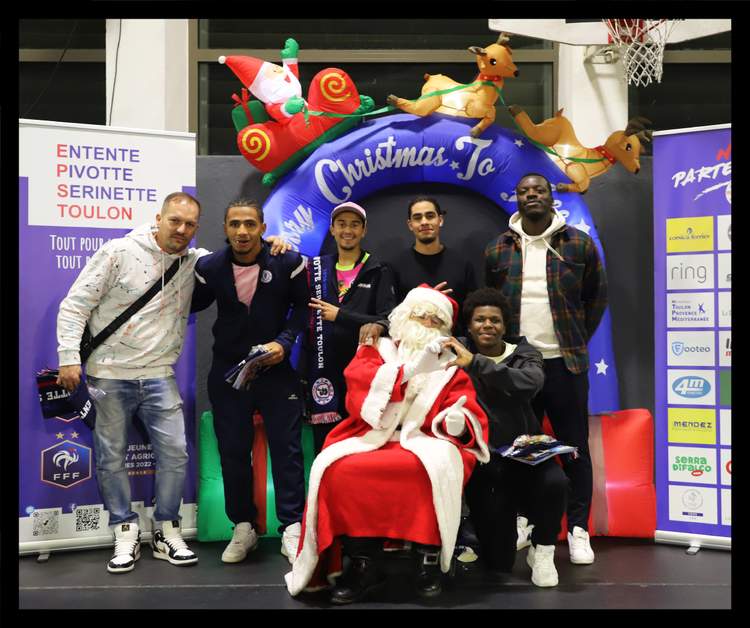 Un groupe de personnes, dont le Père Noël, posent devant une arche gonflable de Noël et des bannières de sponsors.