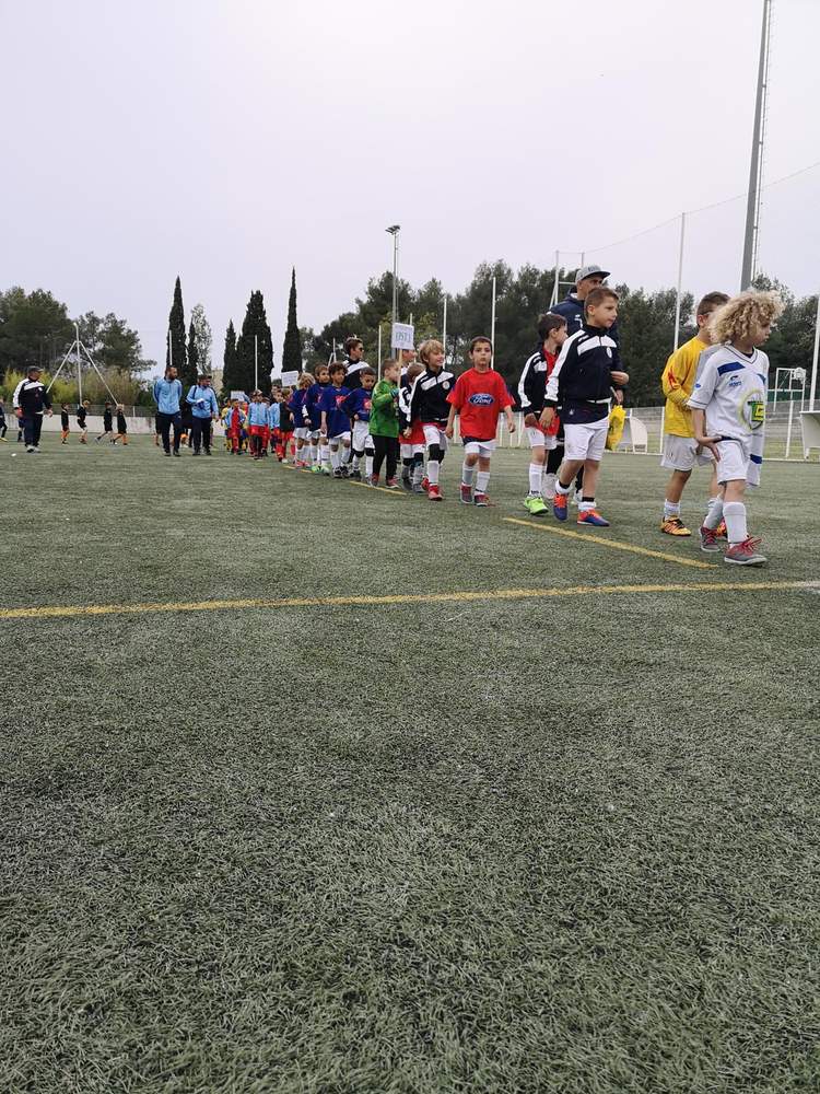 Des jeunes joueurs de football en tenue de sport marchent en ligne sur un terrain en gazon synthétique.