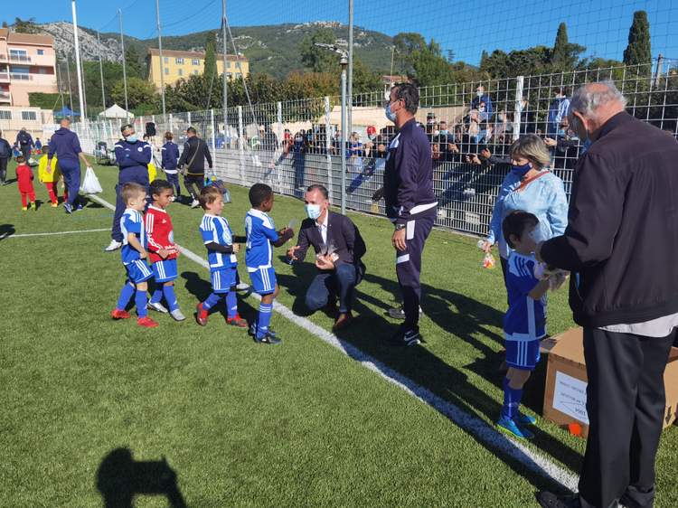 Des jeunes footballeurs reçoivent des récompenses sur le terrain, entourés d'adultes et de spectateurs.