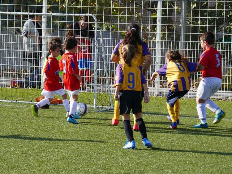 Des jeunes joueurs de football en maillots rouges et jaunes s'affrontent autour d'un ballon sur un terrain en gazon synthétique.