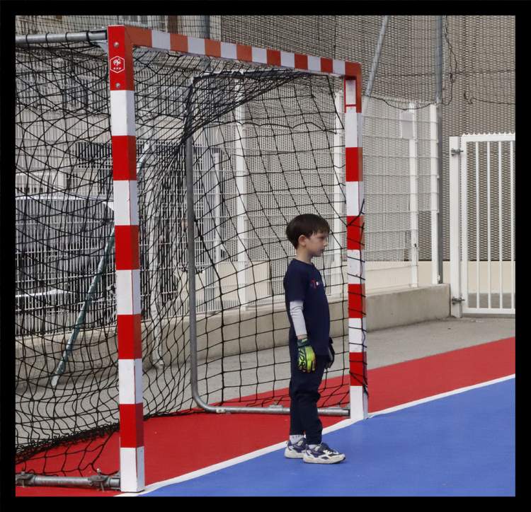 Un jeune enfant en tenue de gardien de but se tient devant un petit but de football sur un terrain coloré.