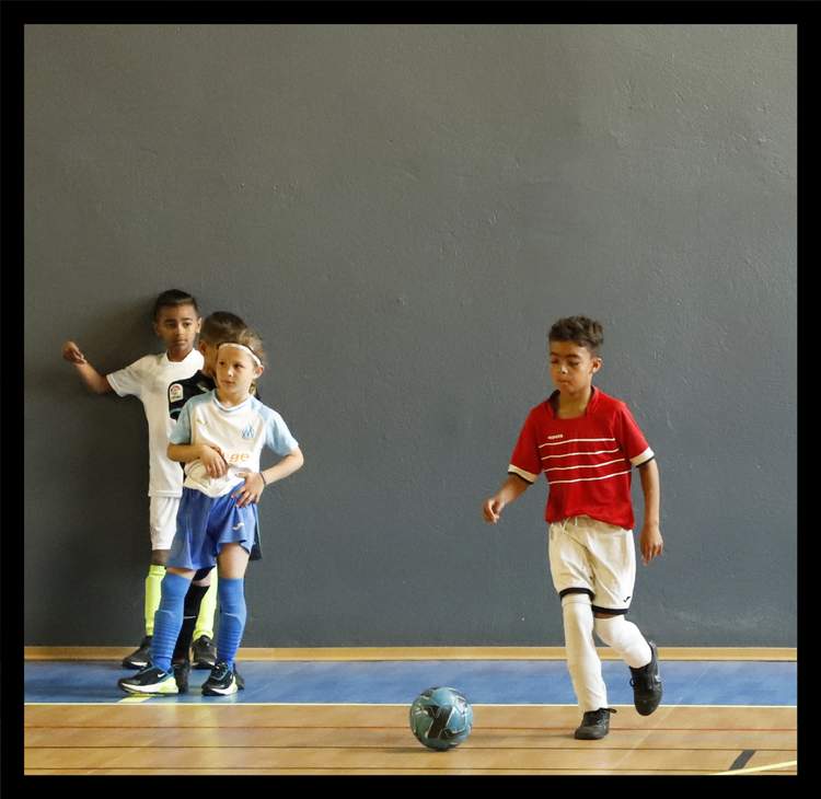 Des jeunes joueurs de football en action sur un terrain de sport en salle.