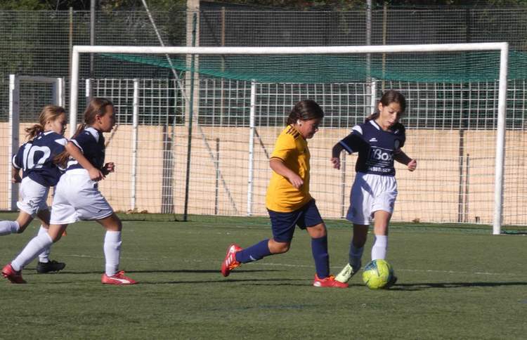 Quatre jeunes joueuses de football en action sur un terrain, avec un ballon près du but.