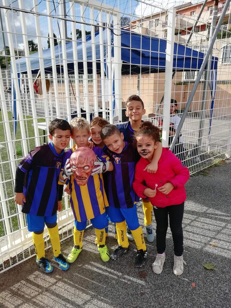 Un groupe d'enfants souriants, dont un portant un masque, posent ensemble sur un terrain de sport.