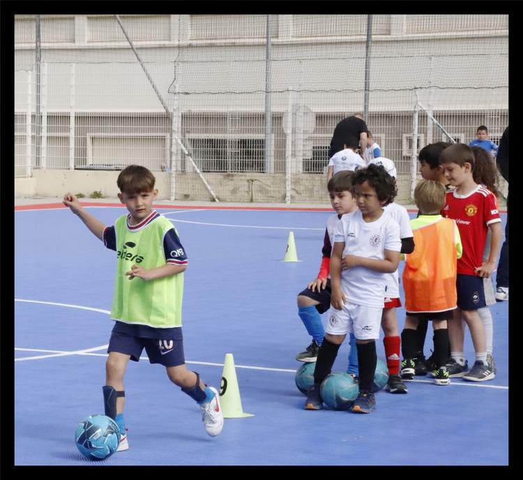 Des jeunes enfants jouent au football sur un terrain bleu avec des cônes.