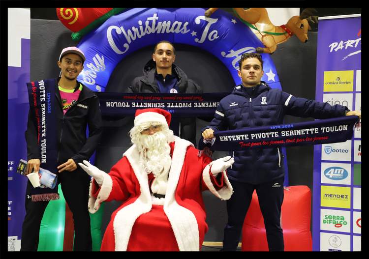 Trois jeunes hommes posent avec le Père Noël devant une arche gonflable de Noël et un panneau de sponsors.