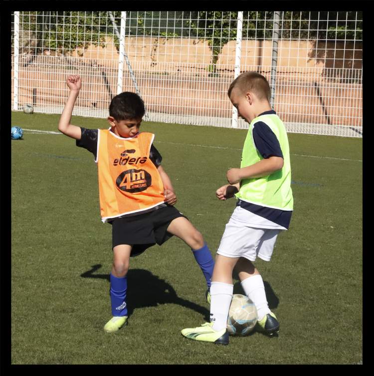 Deux jeunes joueurs de football en pleine action sur un terrain en gazon synthétique.