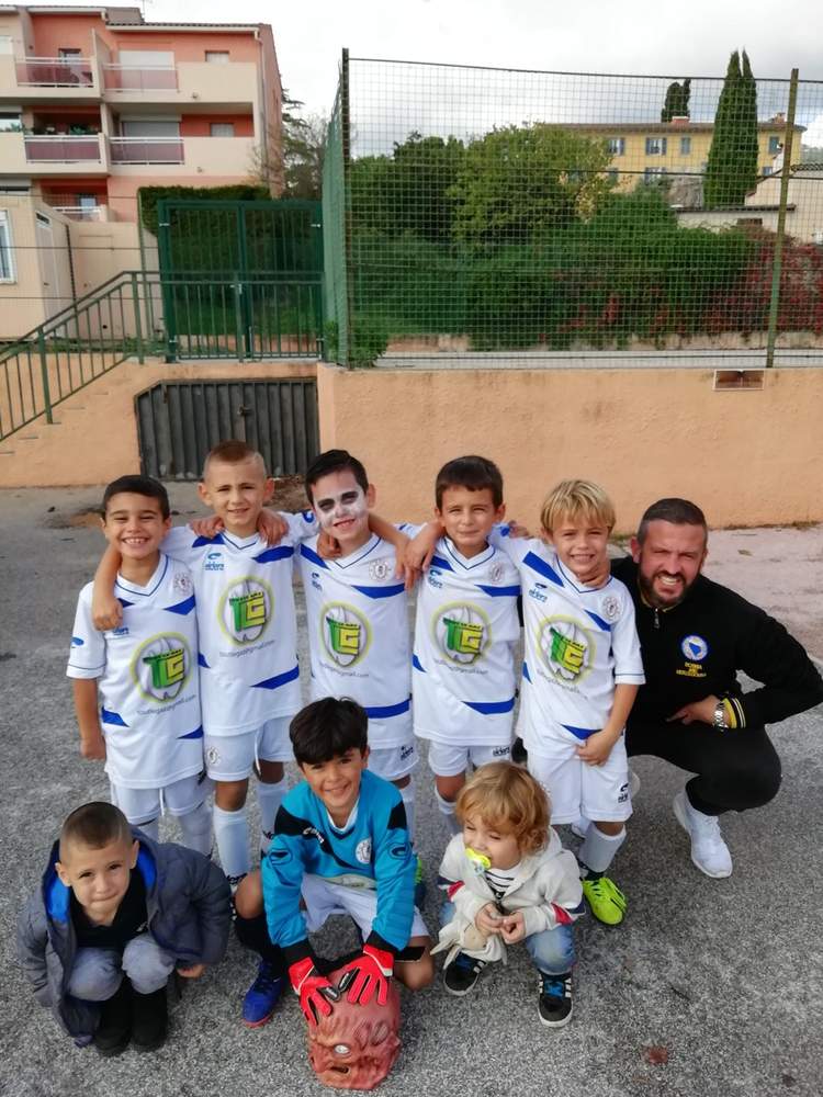 Une équipe de jeunes footballeurs et leur entraîneur posent souriants, avec un enfant déguisé et un bébé.