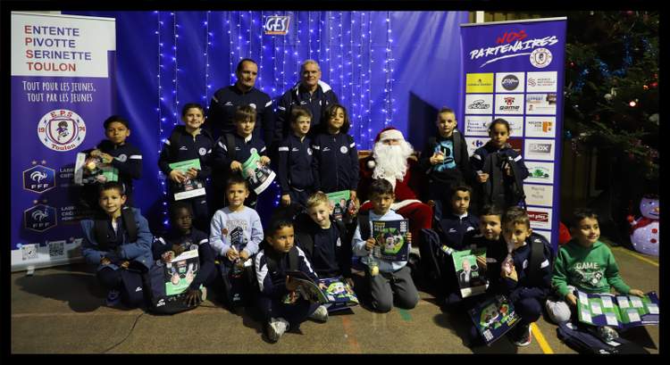 Un groupe d'enfants et d'adultes posent avec le Père Noël devant une banderole et un sapin de Noël.