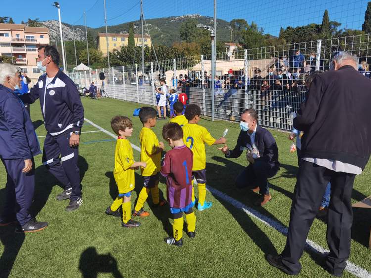 Des jeunes joueurs de football reçoivent des récompenses sur le terrain, sous le regard d'adultes et de spectateurs.