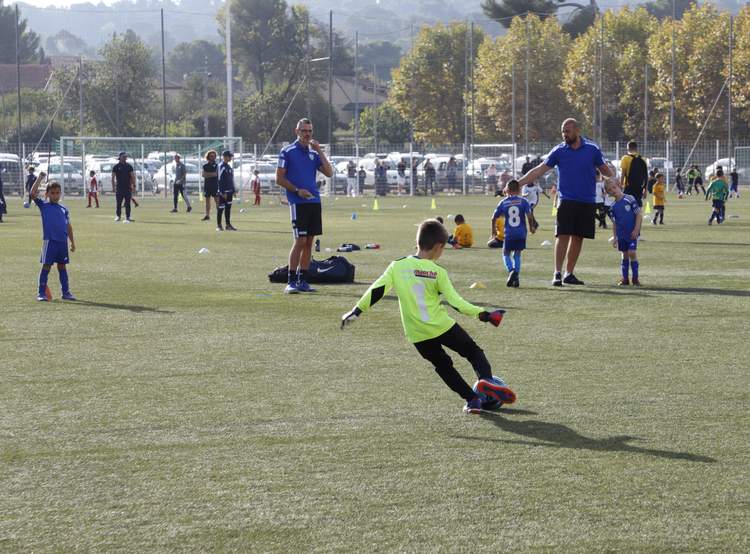 Des jeunes joueurs de football s'entraînent sur un terrain ensoleillé, encadrés par des adultes.
